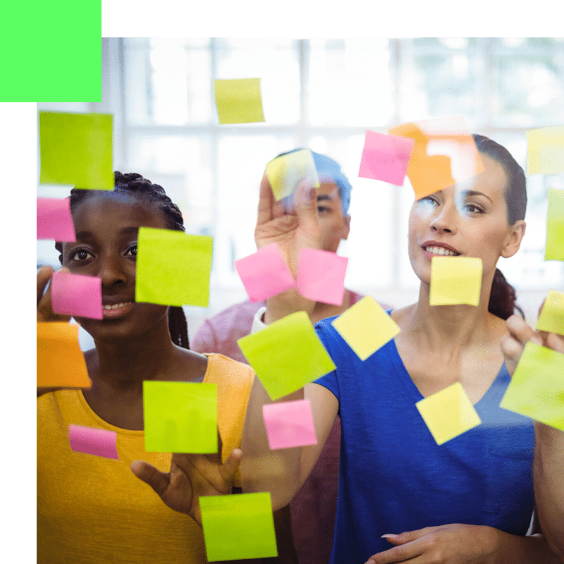 Équipe agile collaborant ensemble, collant des post-it sur un tableau transparent pour organiser et visualiser le processus de travail.