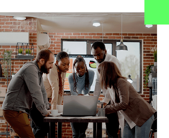 Photo d'une équipe de 5 personnes rassemblée autour d'une table et d'un ordinateur portale travaillant ensemble dans un environnement collaboratif.